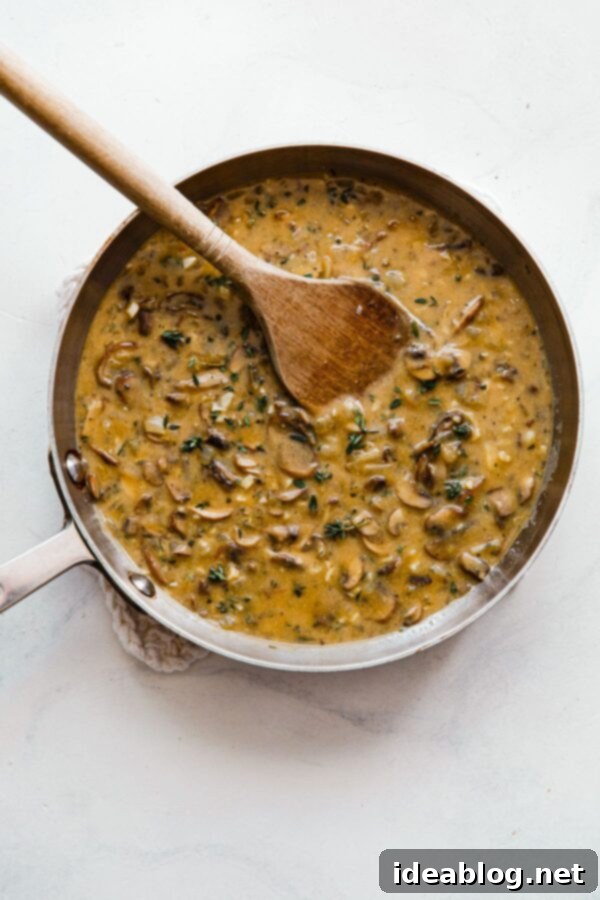 Velvety Vegan Mushroom Gravy 2 Close-up of vegan mushroom gravy simmering in a skillet with a wooden spoon