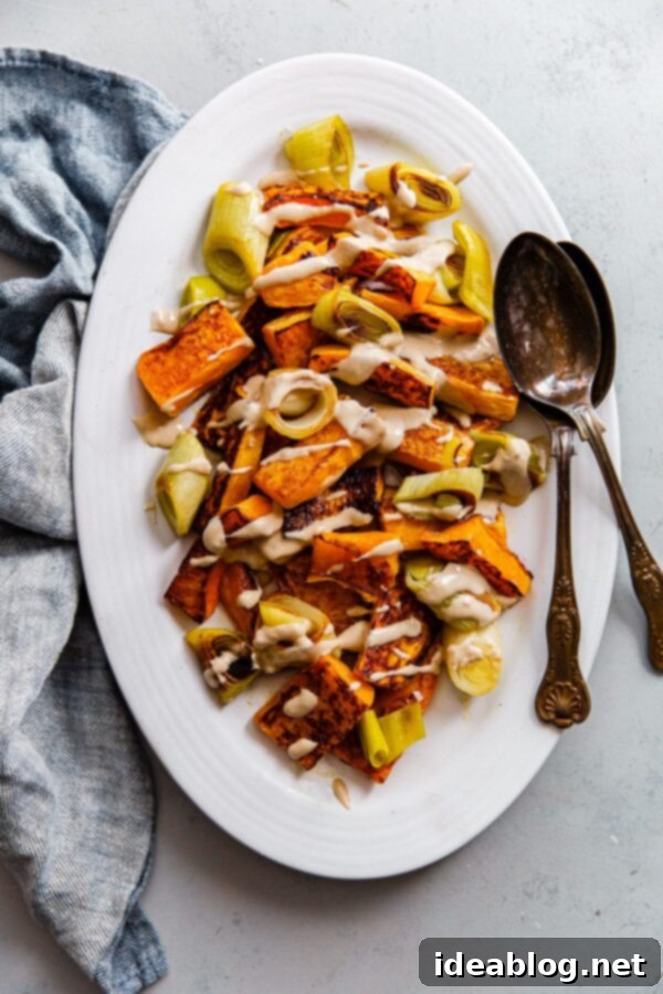 Roasted Butternut Squash and Leeks with Orange Tahini and Za'atar - a delectable vegetarian side dish with warm roasted vegetables, creamy citrus tahini, and crunchy walnut topping. #butternutsquash #leeks #tahini #recipe #sidedish Close-up of roasted butternut squash and leeks glistening with orange tahini sauce, showcasing the textures and colors of the dish.