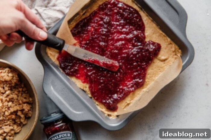Rustic Raspberry Hazelnut Crumb Bake 5 Spreading a rich layer of St. Dalfour Red Raspberry Fruit Spread evenly over the cake batter in a baking pan.