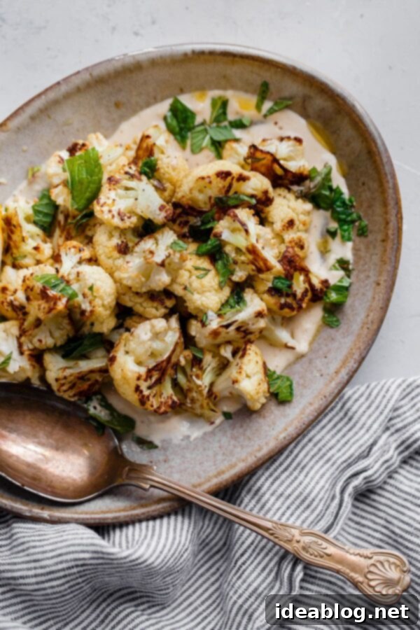 Roasted Cauliflower with Tahini and Mint - a delicious variation on a simple roasted cauliflower recipe! Caramelized and slightly spicy roasted cauliflower florets are served on a lemon tahini sauce and garnished with freshly torn mint leaves and flaky sea salt. Don't be tempted to skip the mint, it adds a lovely bright element to this dish and brings the whole thing together! Serve this roasted cauliflower as a side dish to accompany grilled fish, meat, or other vegetarian main courses. #cauliflower #roastedvegetables #tahini #mint #sidedish #vegetarian #vegan #recipe #abeautifulplate Roasted Cauliflower with Tahini and Mint - a flavorful side dish