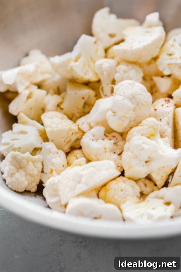Roasted Cauliflower with Tahini and Mint - a delicious variation on a simple roasted cauliflower recipe! Caramelized and slightly spicy roasted cauliflower florets are served on a lemon tahini sauce and garnished with freshly torn mint leaves and flaky sea salt. #abeautifulplate #cauliflower #roastedvegetables #mint #tahini #sidedish #easyrecipes Cauliflower florets in a mixing bowl for seasoning