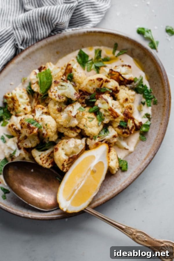 Roasted Cauliflower with Tahini and Mint - a delicious variation on a simple roasted cauliflower recipe! Caramelized and slightly spicy roasted cauliflower florets are served on a lemon tahini sauce and garnished with freshly torn mint leaves and flaky sea salt. #abeautifulplate #cauliflower #roastedvegetables #mint #tahini #sidedish #easyrecipes Plated Roasted Cauliflower with Tahini and Mint garnish