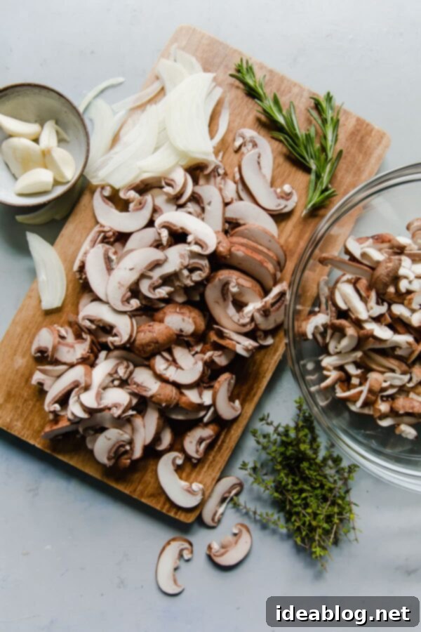 Mushroom Galette - rustic and flavorful, this cremini and shiitake mushroom galette is filled with sharp blue cheese and wrapped in a flaky sour cream pastry dough. This rustic mushroom tart is great for entertaining! #galette #mushroom #tart #cremini #shiitake #recipe #abeautifulplate Sliced Cremini and Shiitake Mushrooms and Onion on Cutting Board with Fresh Rosemary and Thyme