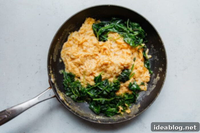 Fluffy Cheesy Eggs with Fresh Greens 8 Folding Cheesy Scrambled Eggs in a skillet, nearly complete